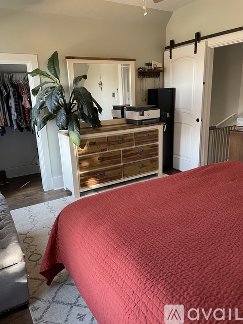 A bedroom with a red bedspread and a wooden dresser with a mirror above it.