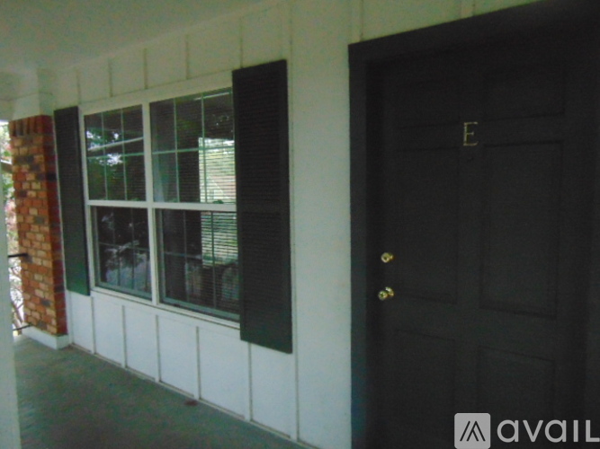 A black door with a gold handle is on the right side of a white wall with a window on the left.