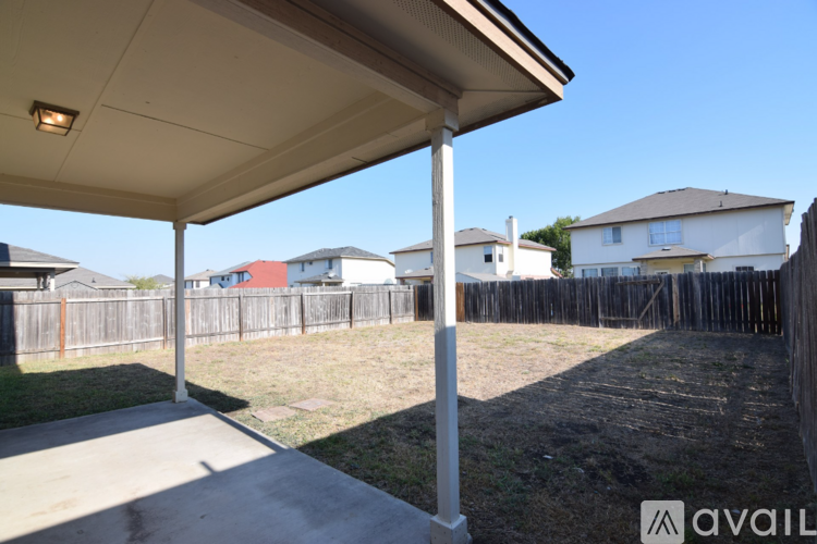 A patio with a white pillar and a roof is in front of a grassy area and a fence.