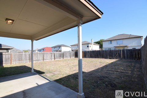 A patio with a white pillar and a roof is in front of a grassy area and a fence.