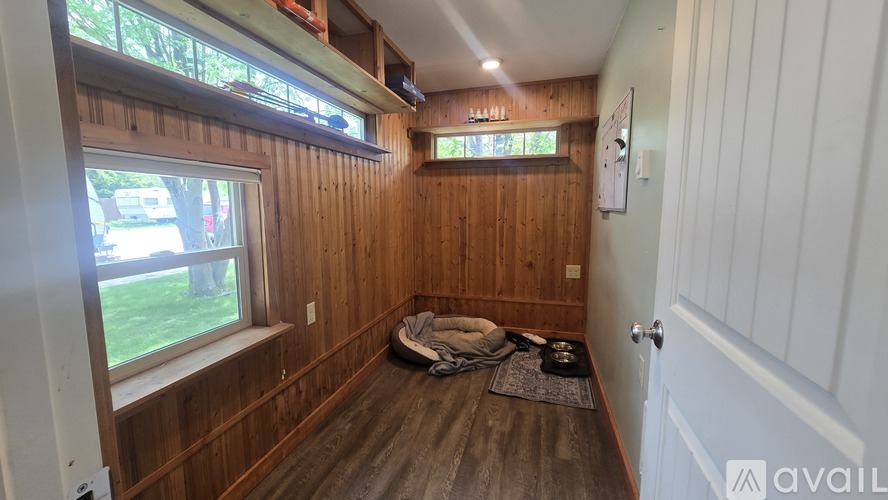 A room with wooden walls and a window with a view of a lawn and trees.