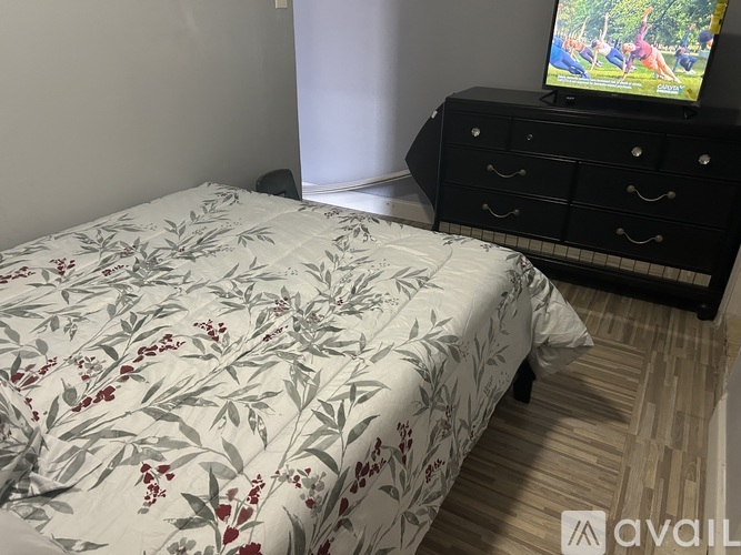 A bed with a floral comforter sits in a room with a TV on a cabinet.