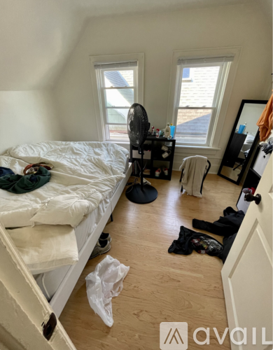 A bedroom with a bed, a fan, a chair, and a window.