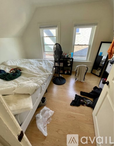 A bedroom with a bed, a fan, a chair, and a window.