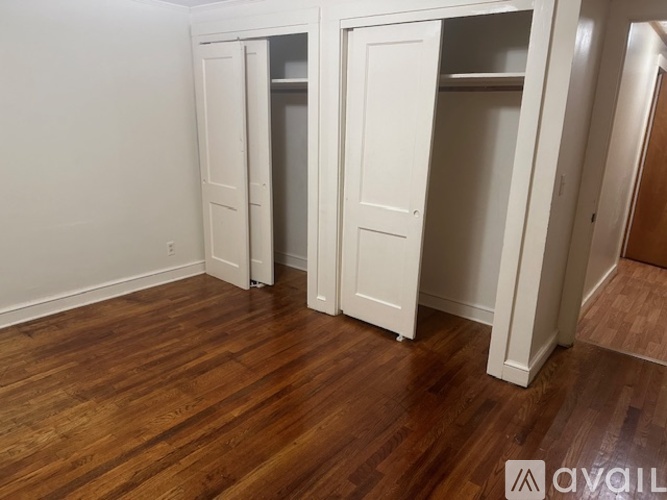 A room with white walls and wooden flooring, featuring a white wardrobe with a door open.