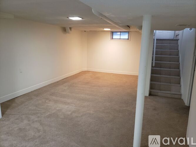 A spacious room with a carpeted floor and a staircase in the background.