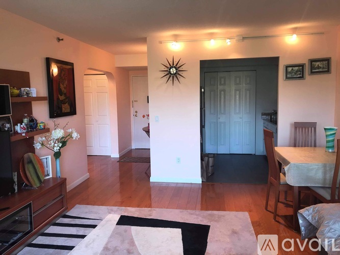 A living room with a black and white rug, a wooden cabinet, a dining table with chairs, and pictures on the wall.