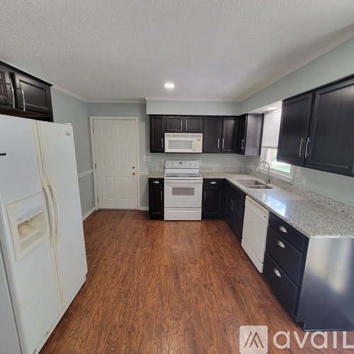 A kitchen with a white fridge, black cabinets, and a wooden floor.