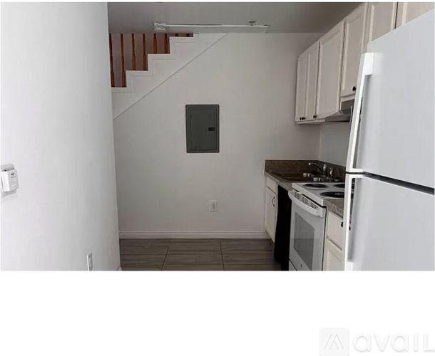 A kitchen with white appliances and a staircase in the background.