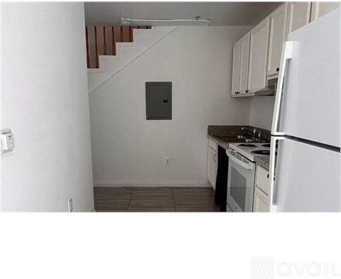 A kitchen with white appliances and a staircase in the background.