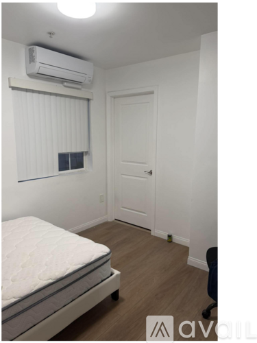 A bedroom with a bed, a window with blinds, a door, and a wall-mounted air conditioner.