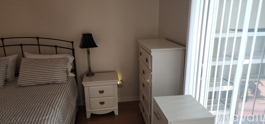 A bedroom with a bed, nightstand, and a window with blinds.