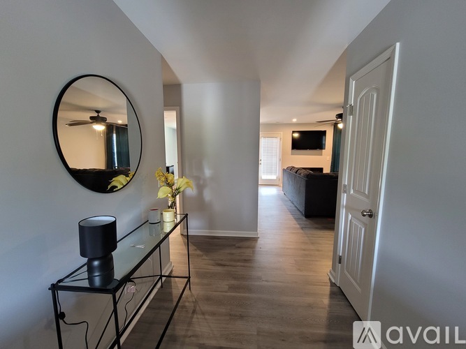 A hallway with a mirror, a table with a lamp and flowers, and a door on the right.