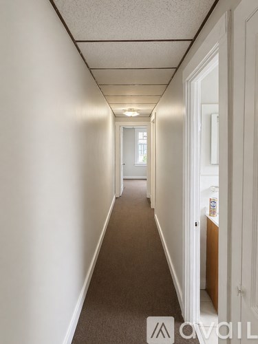 A long hallway with white walls and carpeted floor.