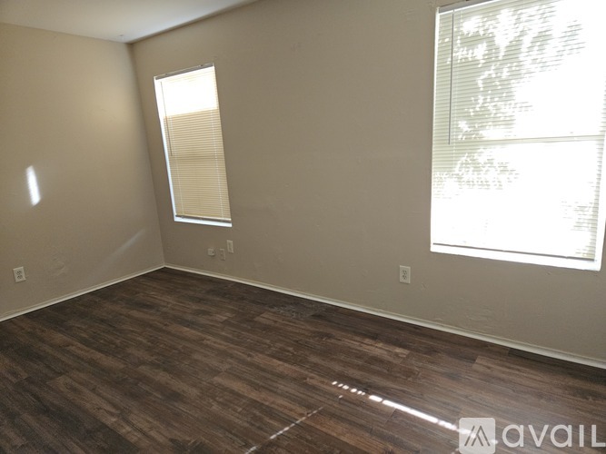 A room with wooden flooring and two windows.