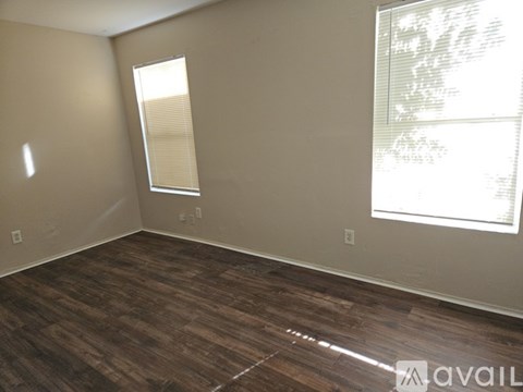 A room with wooden flooring and two windows.