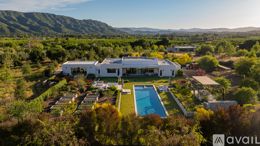 A large white house with a pool in the middle of a green landscape.