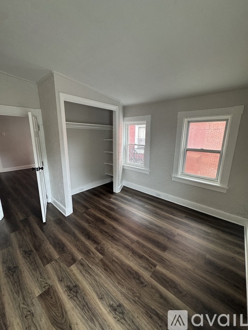 A room with wooden flooring and a window showing a red building outside.