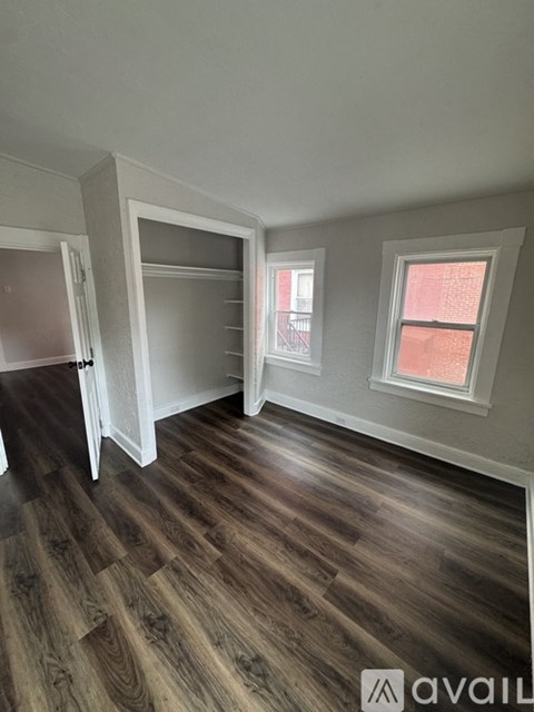 A room with wooden flooring and a window showing a red building outside.