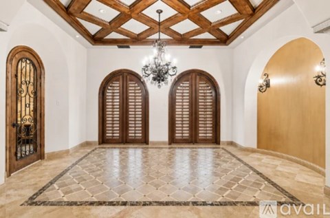 A spacious room with a chandelier, two sets of double doors, and a tiled floor.