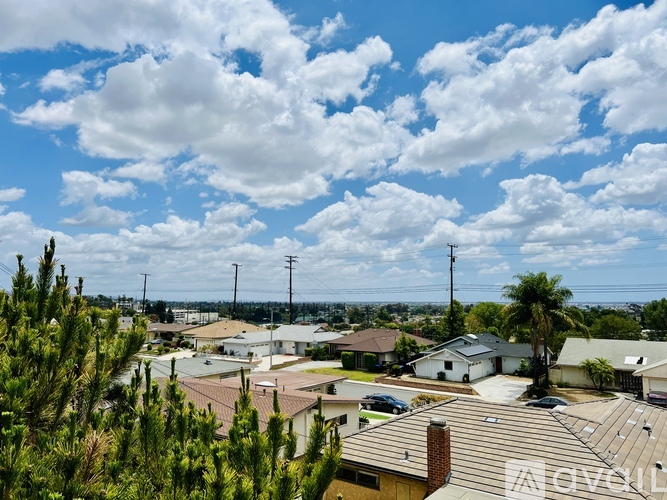 A view of a residential area with houses and trees under a blue sky with clouds.