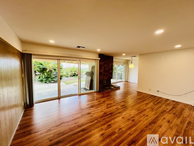 A spacious room with wooden floors and sliding glass doors leading to a garden.