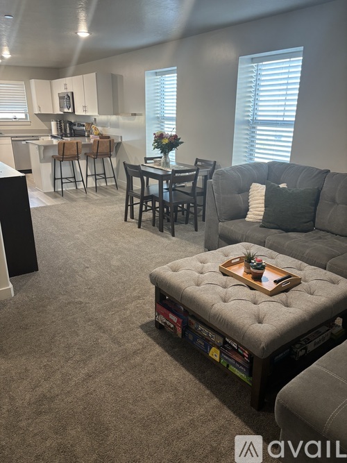 A living room with a grey couch, a coffee table, and a kitchen area in the background.