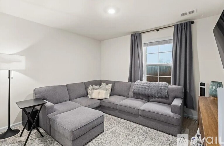 A grey sectional sofa with a small ottoman and a table in front of a window.