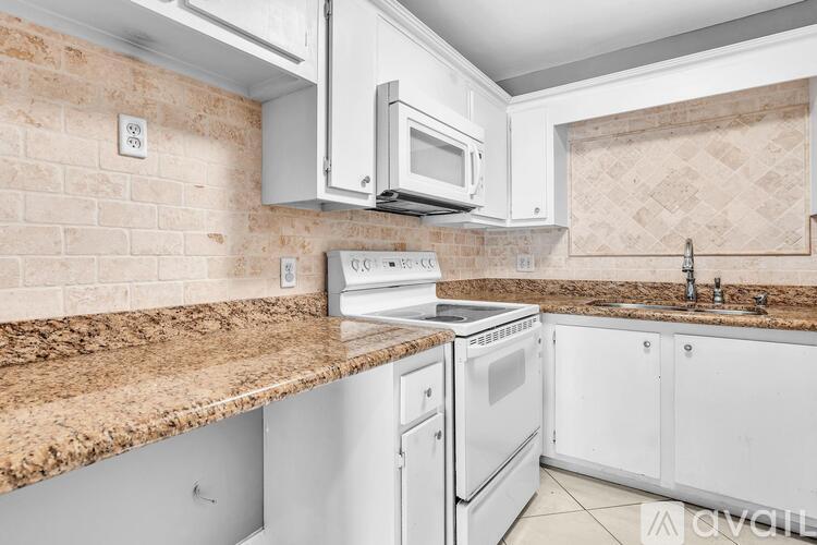 A kitchen with white appliances and a brown granite counter.