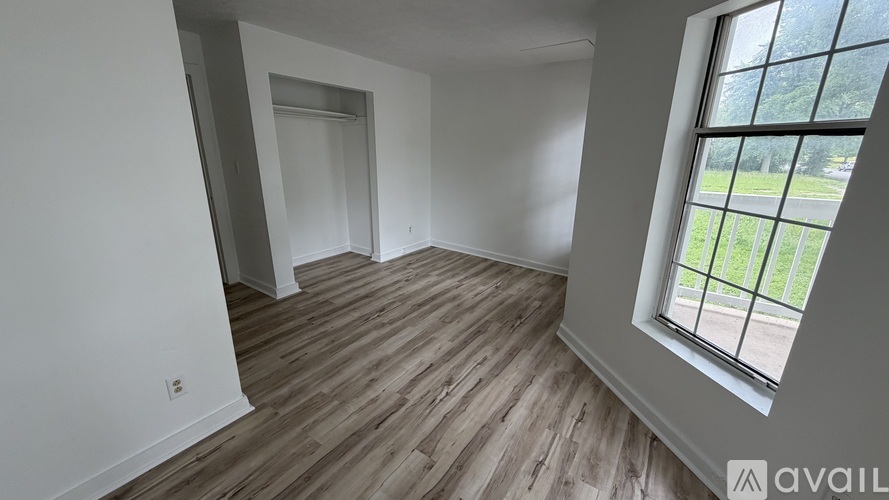 A room with wooden flooring and a window overlooking a green area.