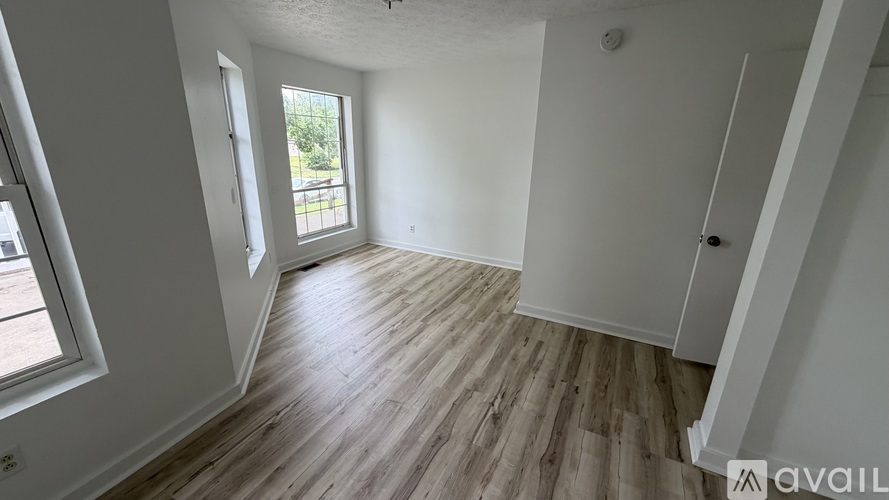 A room with wooden flooring and white walls, with a window and a door visible.