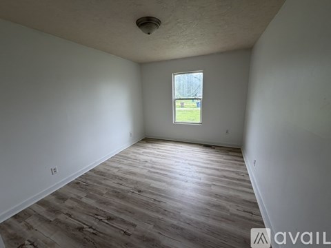 A room with wooden flooring and a window showing a grassy area outside.