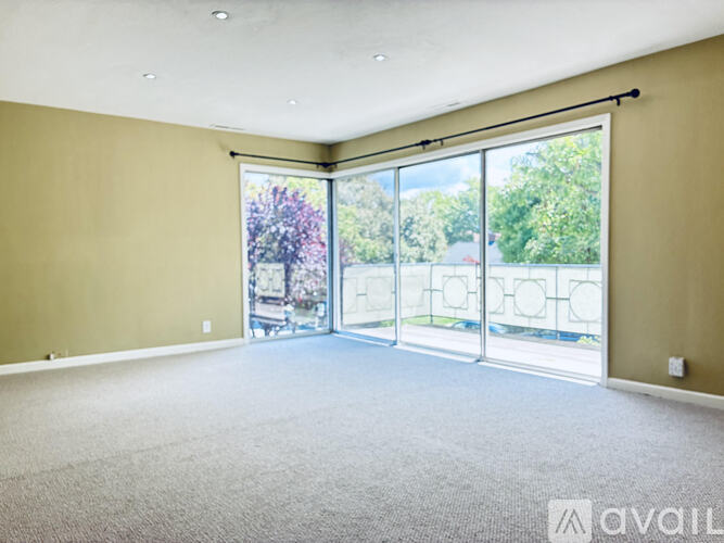 A spacious room with a carpeted floor and sliding glass doors leading to a balcony.
