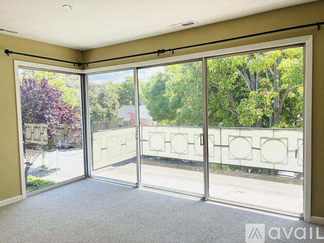 A room with a sliding glass door leading to a balcony with trees and a street view.