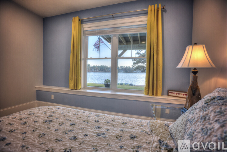 A bedroom with a bed, a window with yellow curtains, and a lamp on a nightstand.