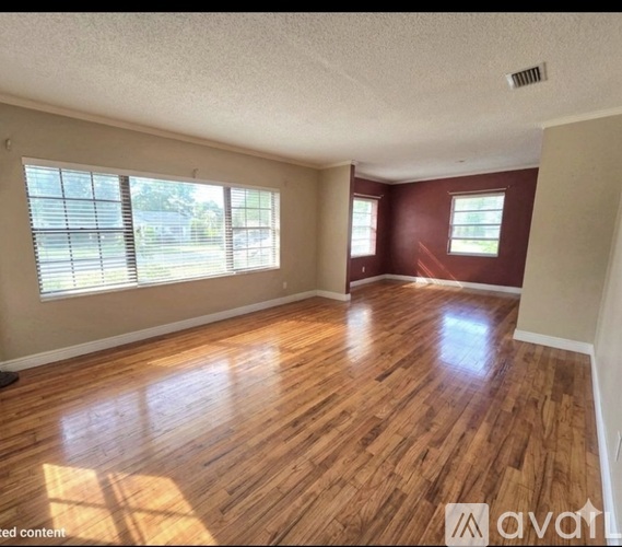 A room with wooden flooring and two windows.