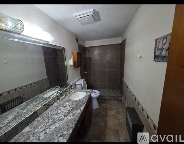 A bathroom with a granite countertop and a toilet in the corner.