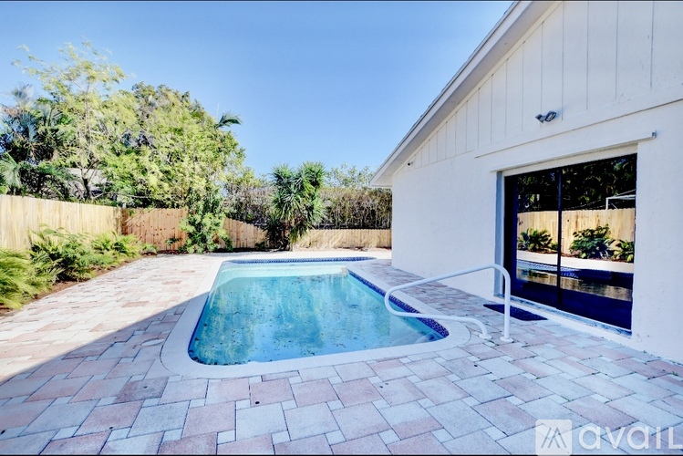 A pool surrounded by a brick patio in front of a white building.