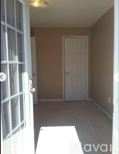 A white door is open to a hallway with a white table and a white door in the distance.