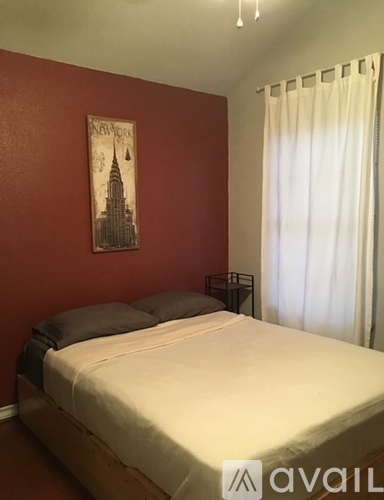 A bedroom with a bed, a poster on the wall, and a window with curtains.
