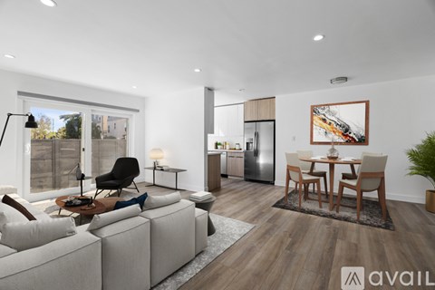 A modern living room with a grey sofa, a black chair, a wooden dining table and chairs, and a kitchen area in the background.
