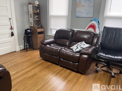 A brown leather couch sits in a living room with a wooden floor and a black office chair.