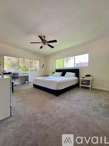 A bedroom with a bed, desk, and ceiling fan.
