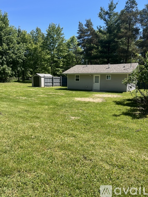 A house with a grey roof and a white door is surrounded by a grassy field.