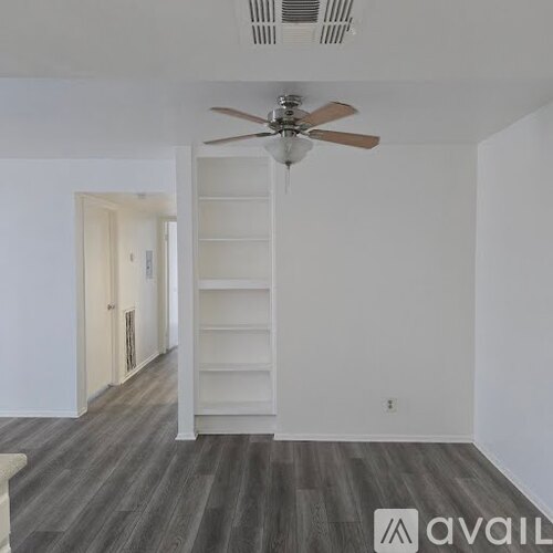 A room with a fan and a wooden floor.