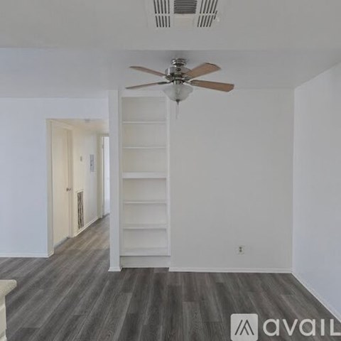A room with a fan and a wooden floor.