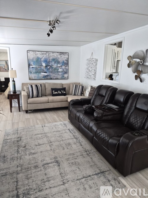 A living room with a black leather couch and a grey rug.