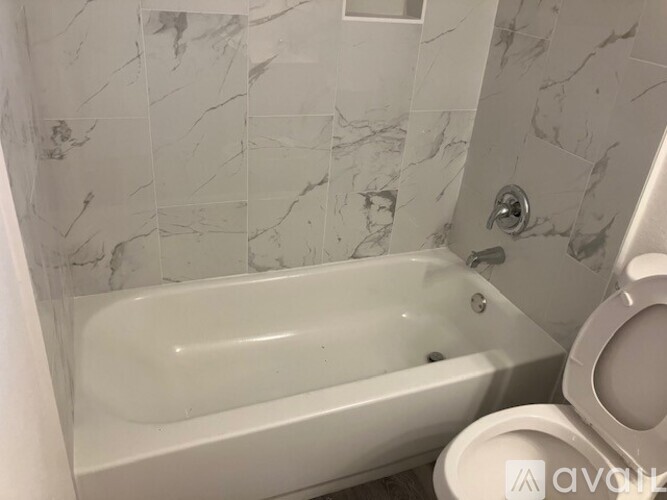 A white bathtub sits in a bathroom with marble tile walls.