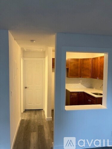A hallway with a white door and a view into a kitchen.