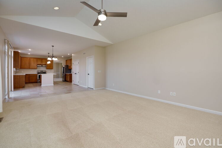 A spacious living room with a kitchen in the background and a carpet on the floor.